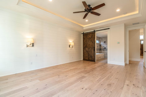 Heights at Pleasant Valley Lot 48 master bedroom with ceiling fan, ship lap wall with sconces, sliding barn door to master bathroom
